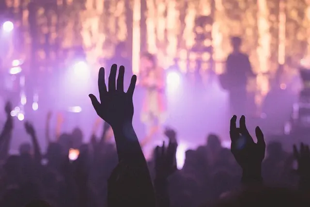 Hands raised in a crowd under purple stage light