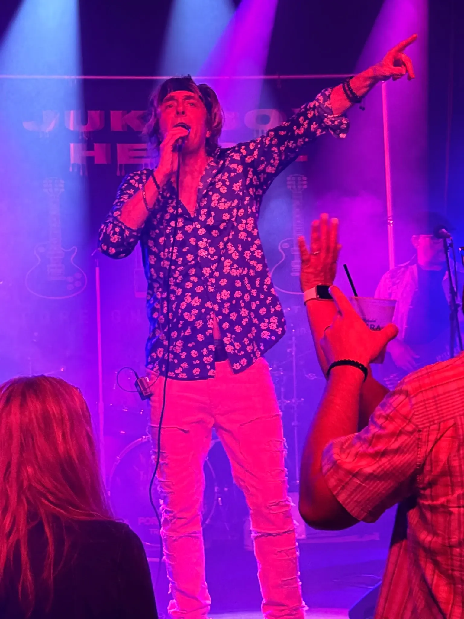 Jukebox Hero'z singer pointing to the crowd mid-song under purple stage light, hands raised in front of him