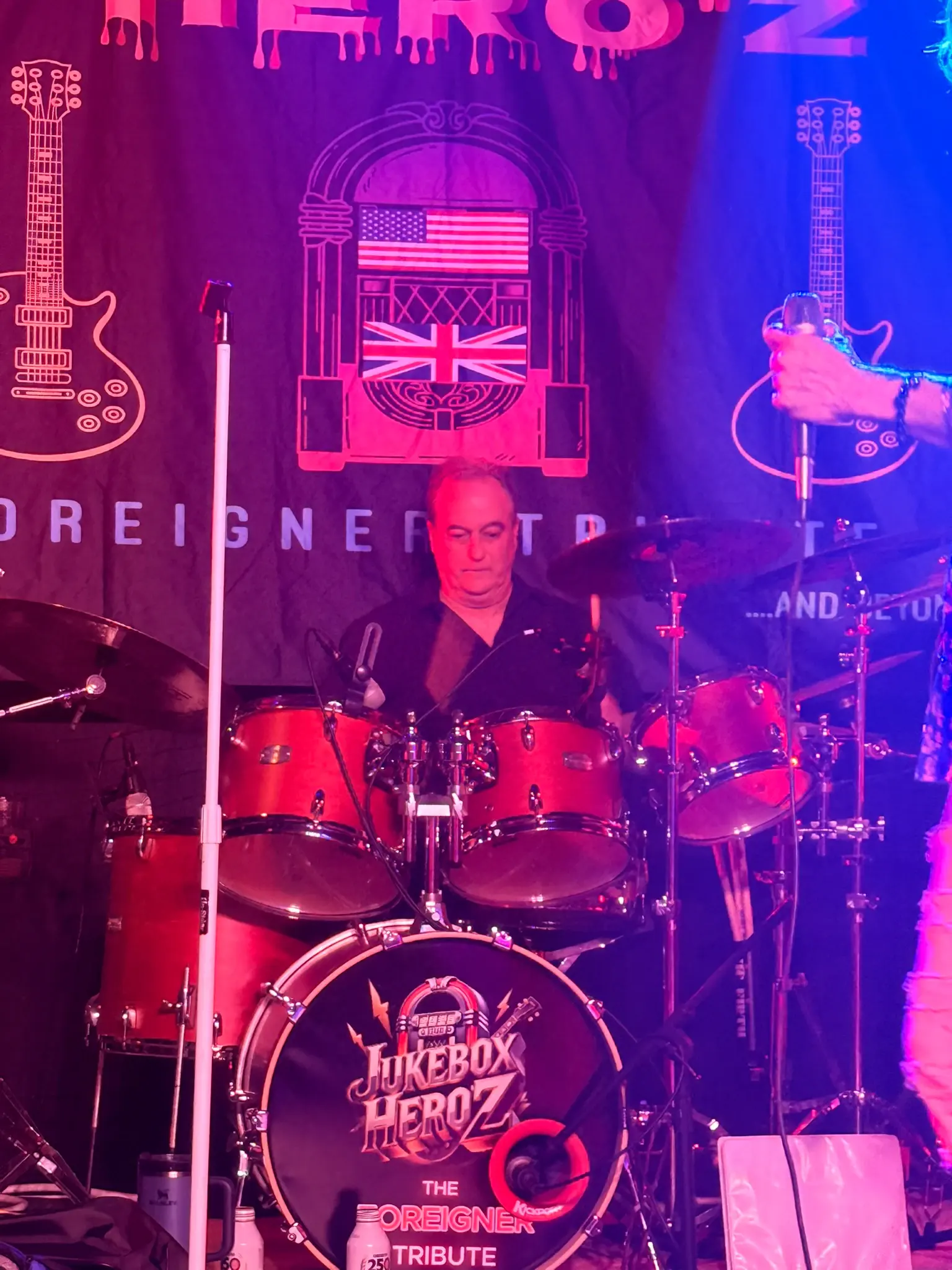 Jukebox Hero'z drummer behind a red kit, in front of the band's Foreigner Tribute banner