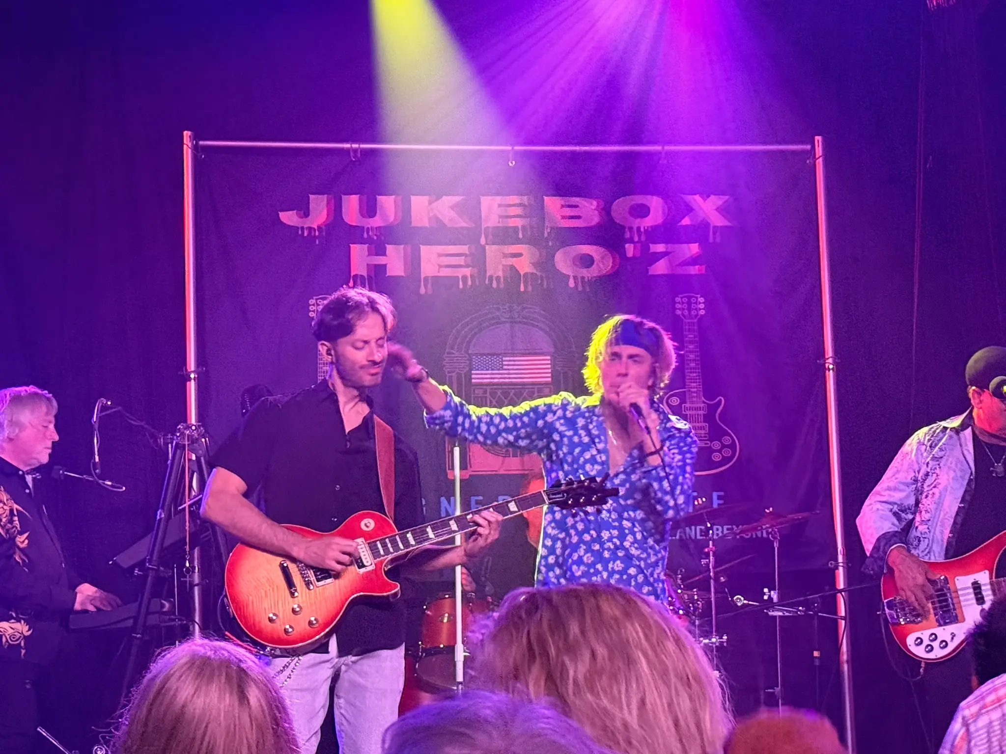 Jukebox Hero'z guitarist and singer performing together in front of the band's banner, with the keyboard player and bassist either side